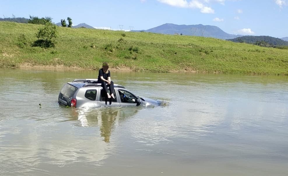 Rapaz fica calmo em cima do teto de automóvel ao cair em rio