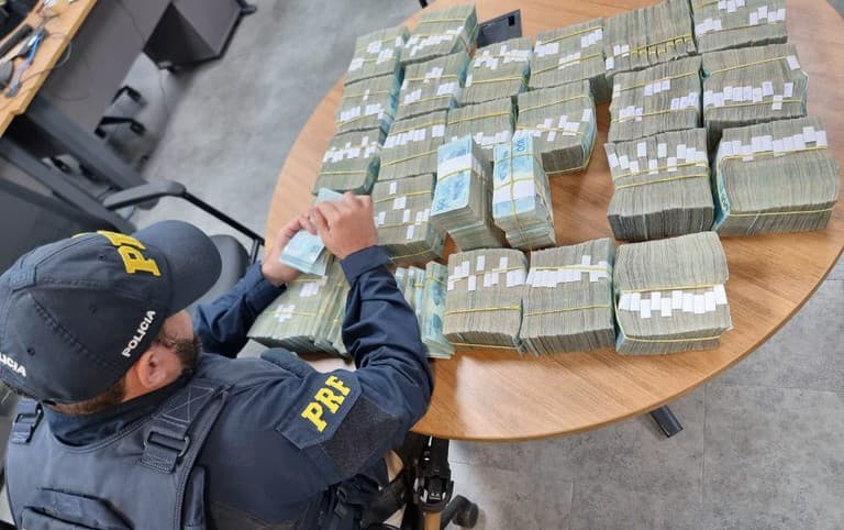 Policial contando notas de cem apreendidas (Foto: PRF)